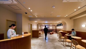 A modern interior with a reception desk, wooden tables, and chairs, and a pool table in the background. - Hotel Plus Hostel TOKYO ASAKUSA 2 (Tokyo)