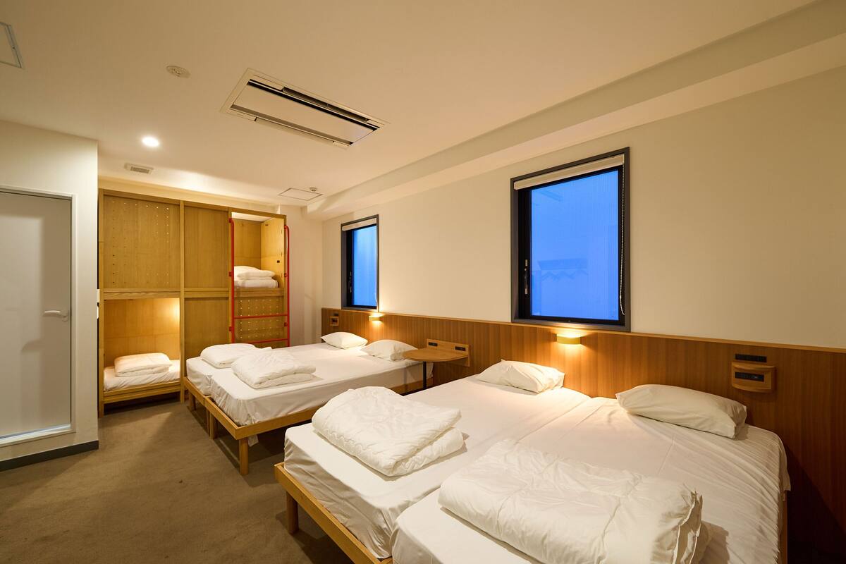 A hotel room with two single beds, a wooden wardrobe, a built-in closet, and a window with a view.