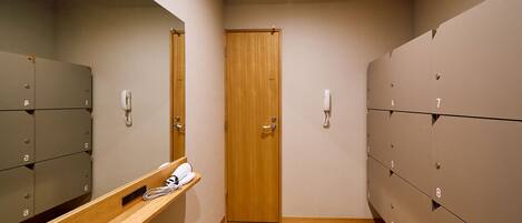A narrow hallway with lockers on both sides, a wooden door at the end, and a mirror on the left wall.
