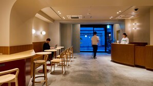 A modern interior with round tables and wooden chairs, a reception desk, and a view of the street outside. - Hotel Plus Hostel TOKYO ASAKUSA 2 (Tokyo)