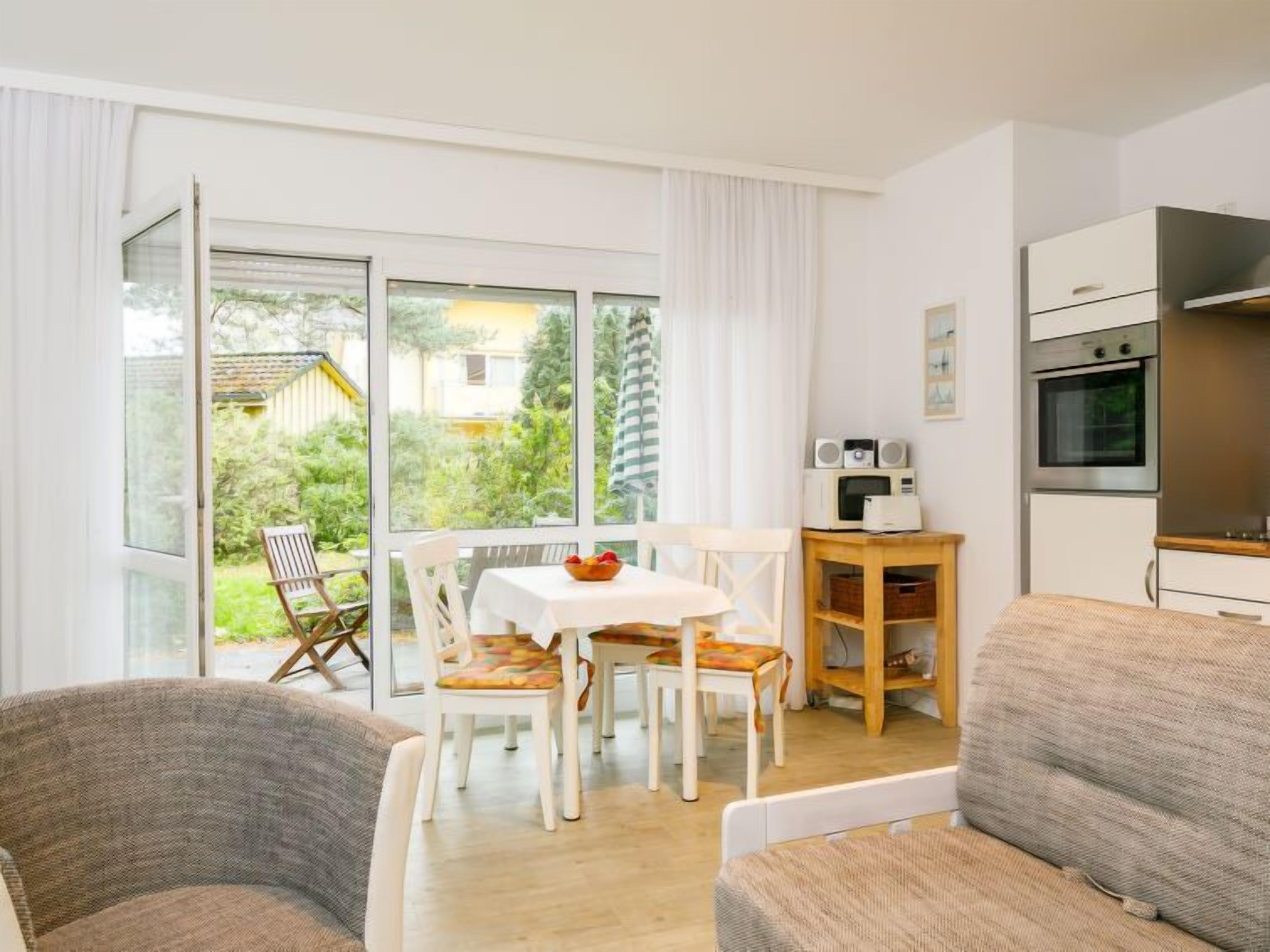 A modern living room with a dining area, a kitchen with appliances, and a view of the garden.