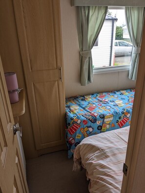 Un dormitorio con cama, armario, ventana con cortinas y vista a un coche estacionado afuera.