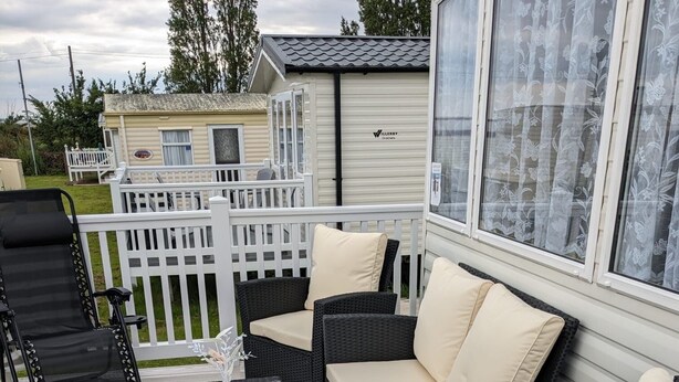 A covered outdoor seating area with wicker furniture and a glass table. - Pet friendly 2 bed caravan in coopers beach (Mersea Island)