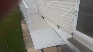 A residential building with a covered porch, a metal ramp leading to the entrance, and a small step at the bottom. - Pet friendly 2 bed caravan in coopers beach (Mersea Island)