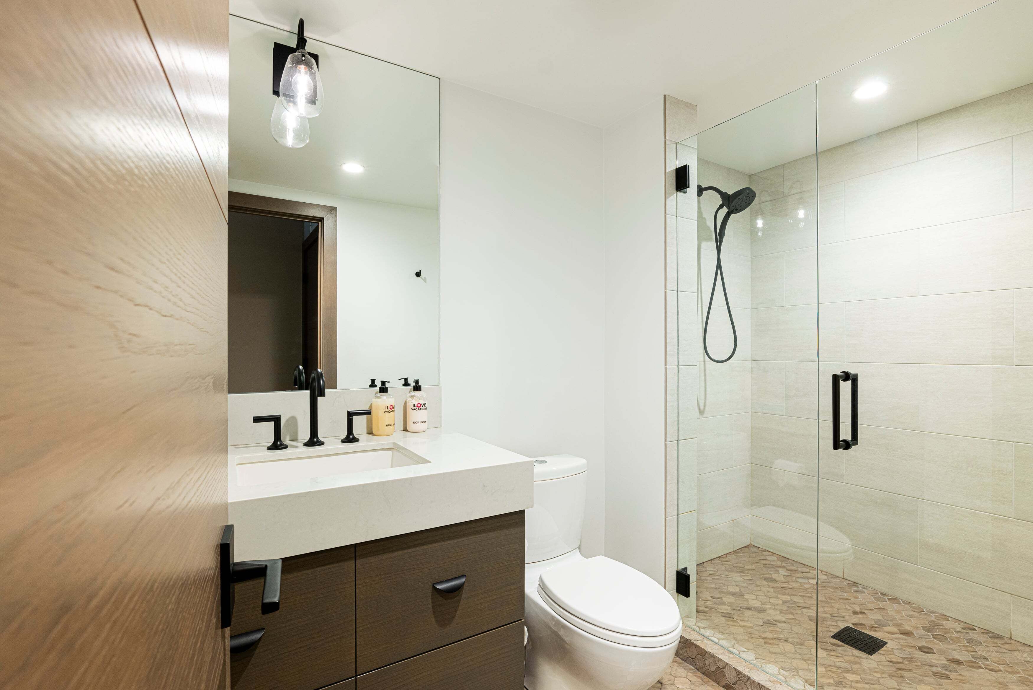 Une salle de bain moderne avec une douche à parois de verre, des toilettes blanches et un meuble-lavabo en bois avec un miroir.