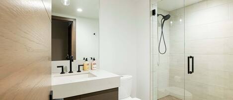 Une salle de bain moderne avec une douche à parois de verre, des toilettes blanches et un meuble-lavabo en bois avec un miroir.