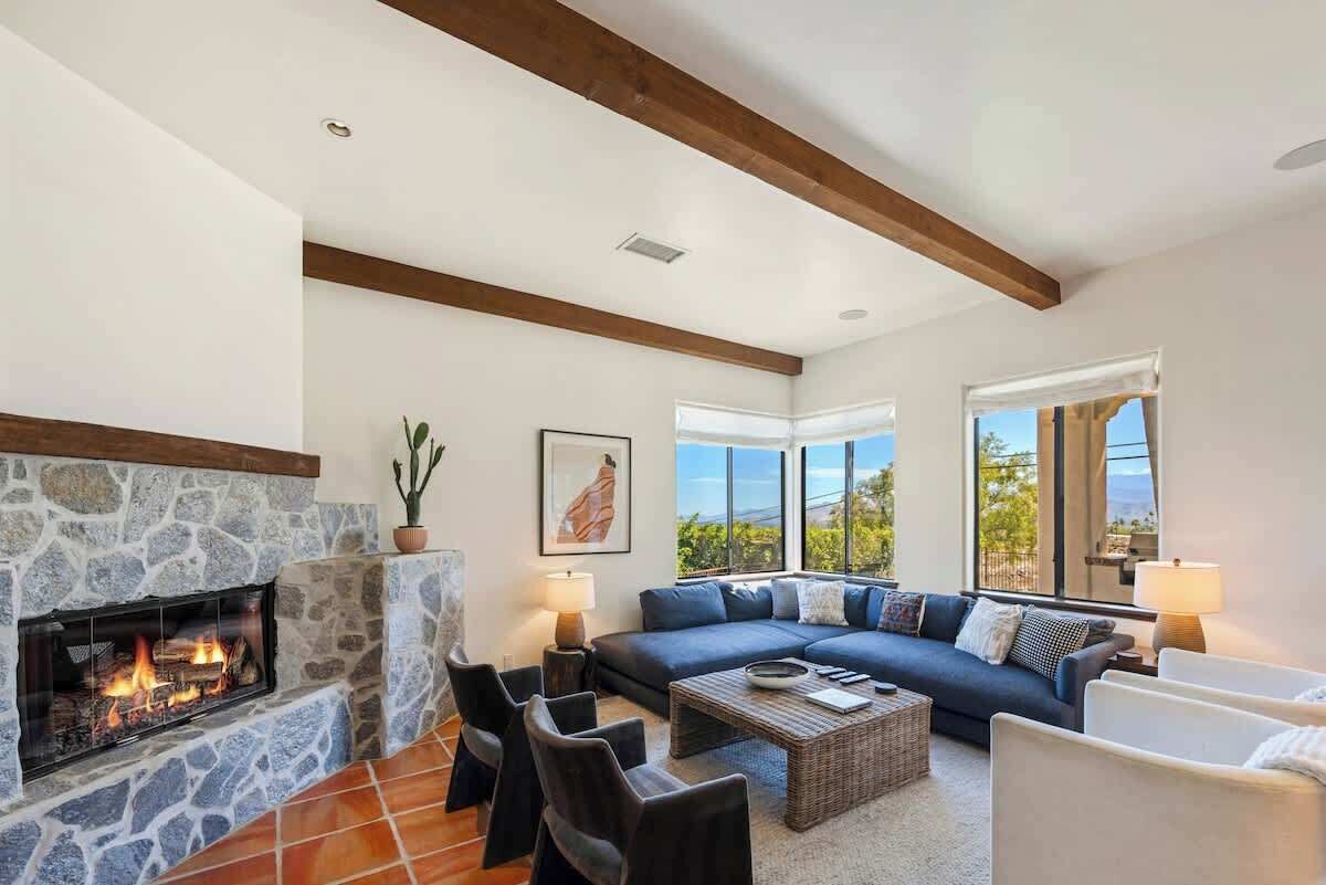 A living room with a stone fireplace, a dark blue sofa, and a view of the outdoors.