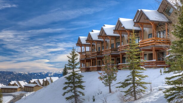 A snow-covered lodge with multiple wooden balconies and a mountainous backdrop. - Saddle Ridge Ski in/Ski out condo, private hot tub (Big Sky)
