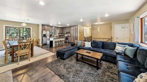 A spacious living room with a dark-colored sofa, a wooden dining table with chairs, and a kitchen area in the background. - Family Cabin with Hot Tub and Game Room (South Lake Tahoe)