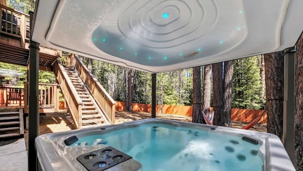 A hot tub with a ceiling light, surrounded by a wooden deck and trees. - Family Cabin with Hot Tub and Game Room (South Lake Tahoe)
