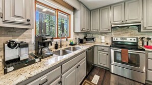 A modern kitchen with granite countertops, stainless steel appliances, and a large window with a view of trees. - Family Cabin with Hot Tub and Game Room (South Lake Tahoe)