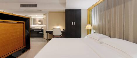 Habitación de hotel con una cama grande, un escritorio con silla, un armario y un baño a simple vista.