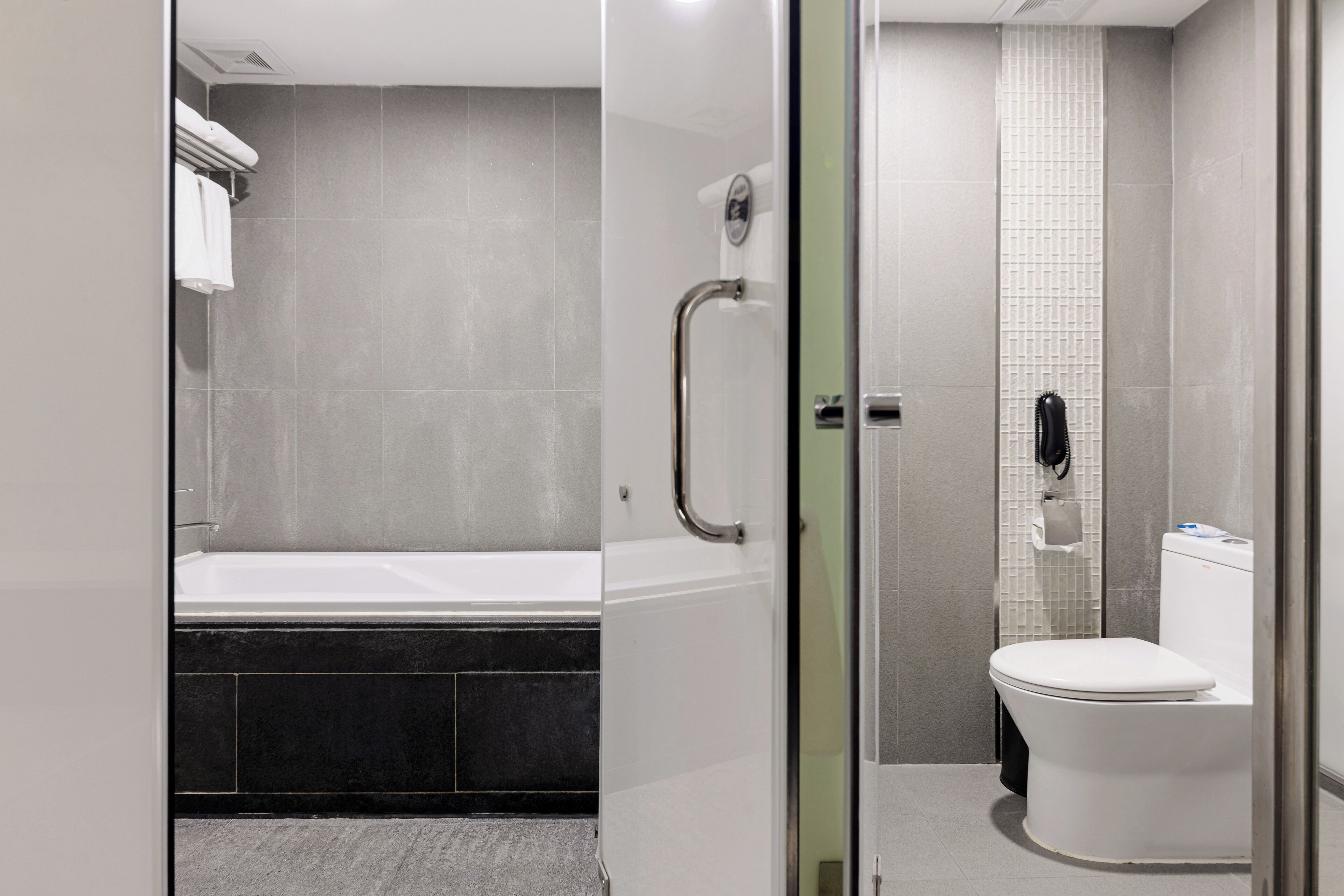 A modern bathroom with a bathtub, toilet, and glass shower enclosure.
