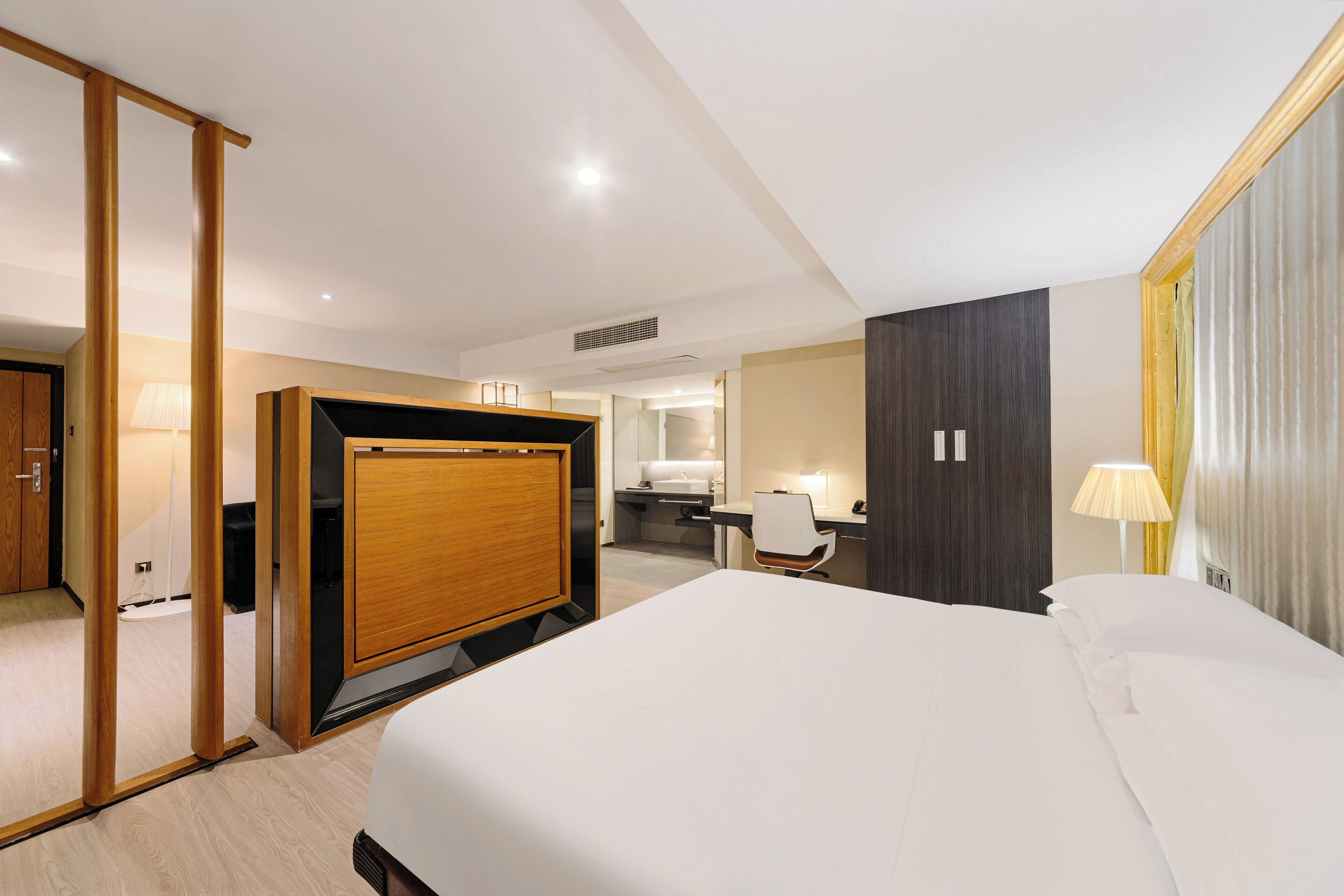 A hotel room with a bed, a desk, a chair, a wardrobe, and a bathroom visible through an open door.
