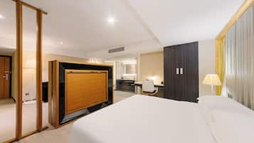 A hotel room with a bed, a desk, a chair, a wardrobe, and a bathroom visible through an open door.