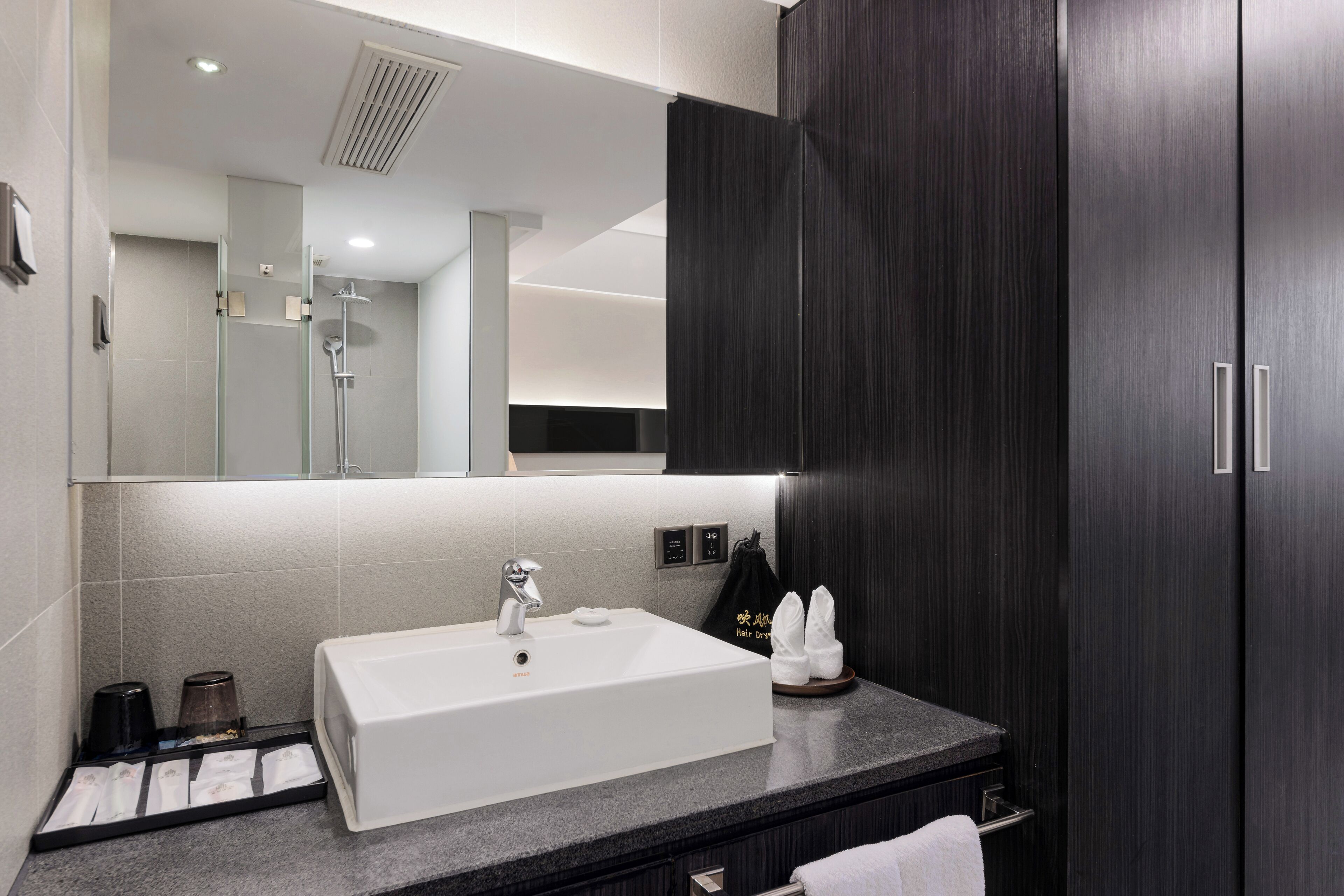 A modern bathroom with a white sink, dark wood cabinets, and a large mirror.