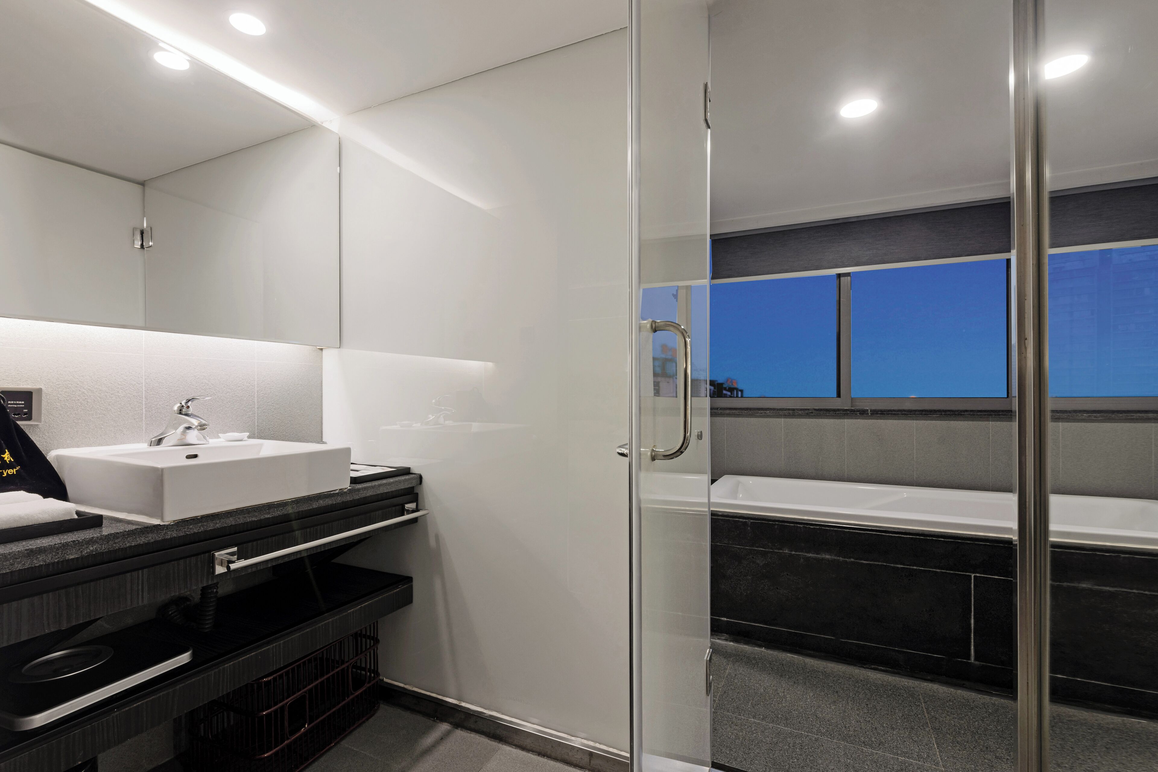 Un bagno moderno con cabina doccia in vetro, lavandino bianco e piano di lavoro nero.