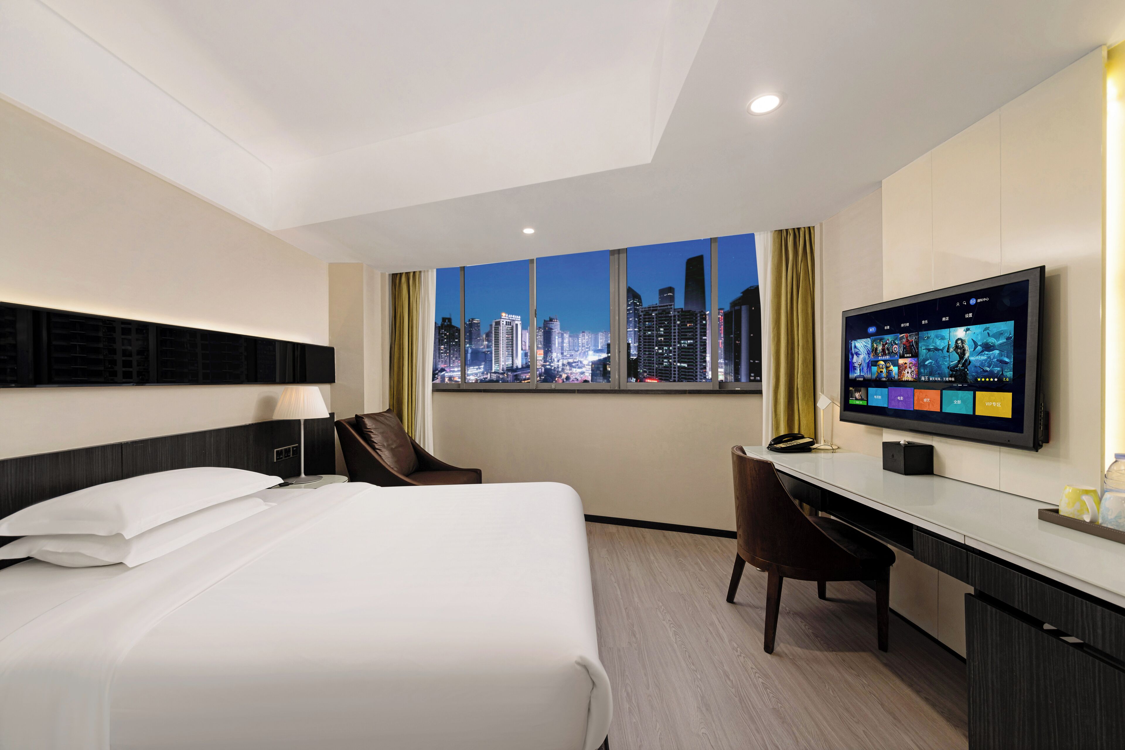 A hotel room with a bed, desk, chair, TV, and a city view.