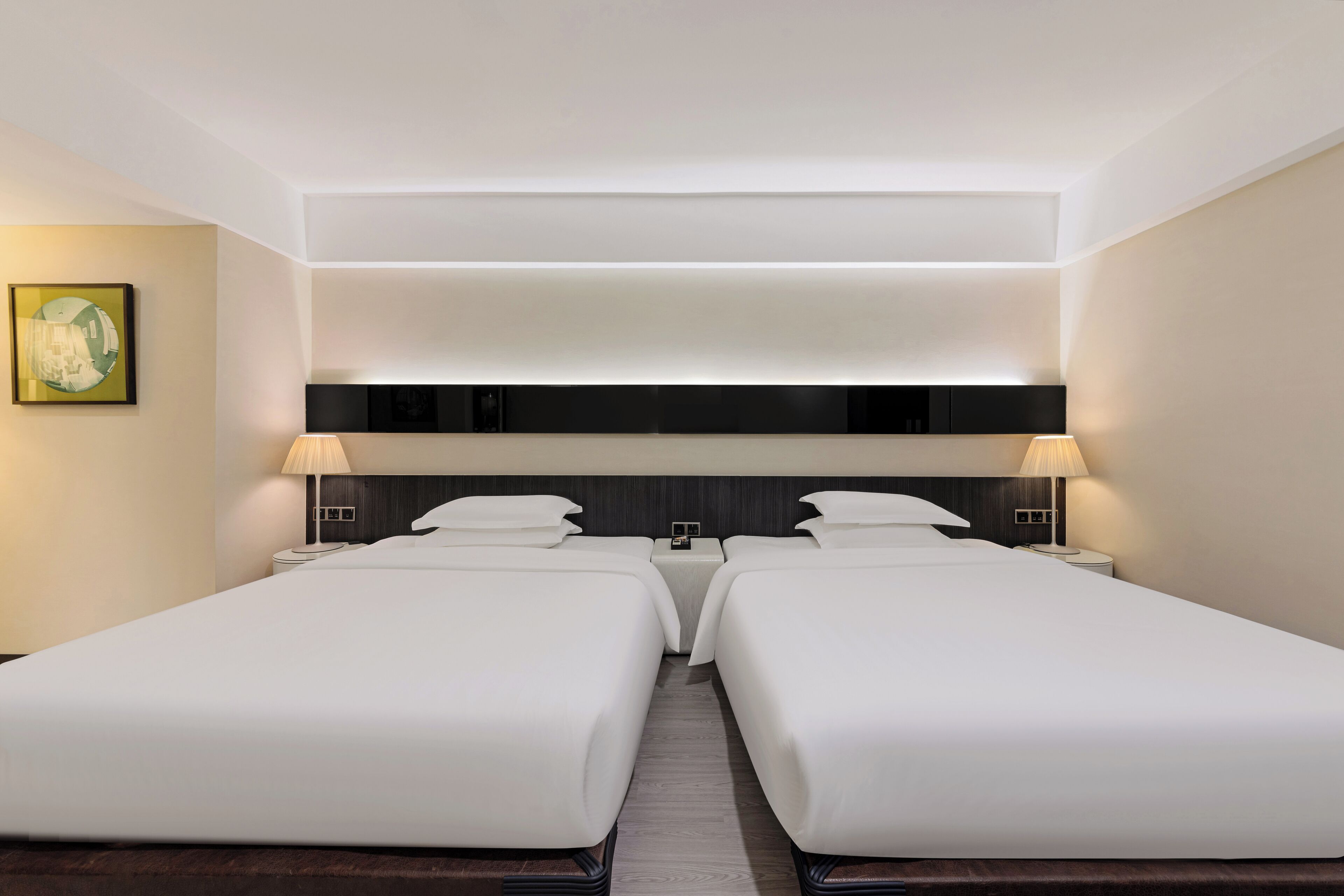 Habitación de hotel con dos camas individuales, cabecero de madera oscura, televisor montado en la pared y una mesita de noche con lámpara.