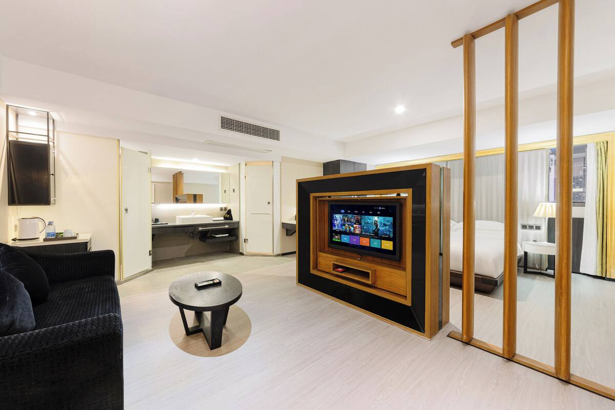 A modern hotel room with a flat-screen TV, a sofa, a small round table, a bed, and a sliding door.