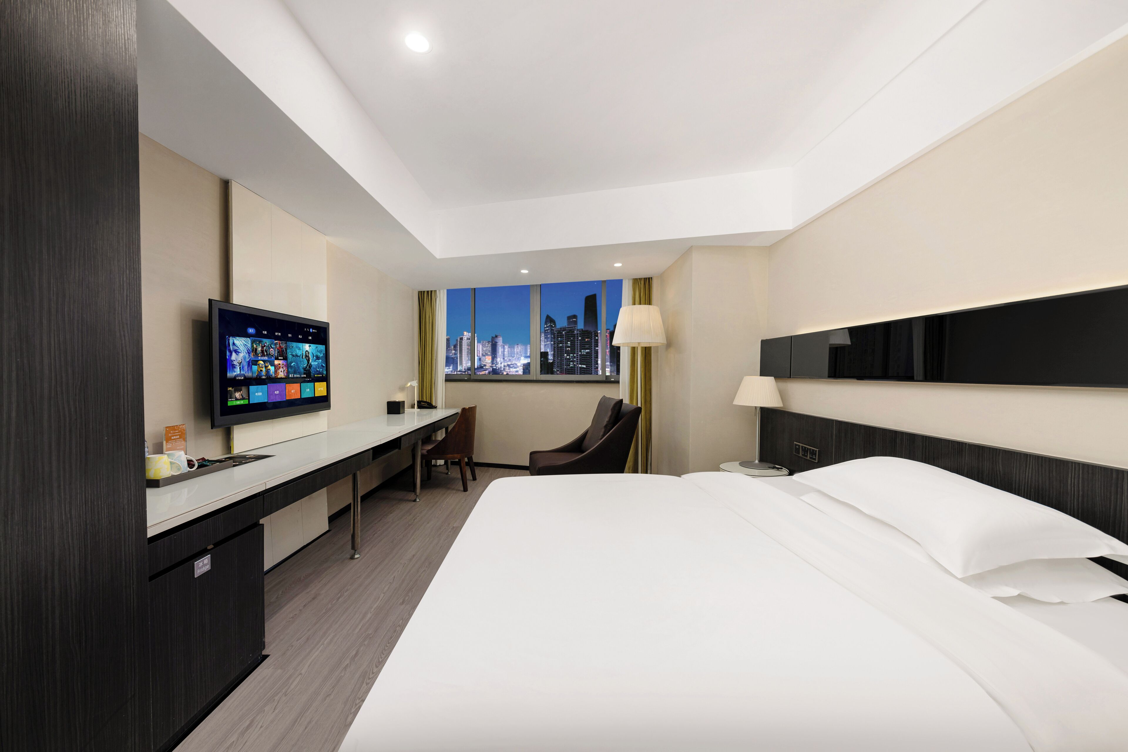 A modern hotel room with a large bed, a desk with a flat-screen TV, a chair, and a window with a city view.