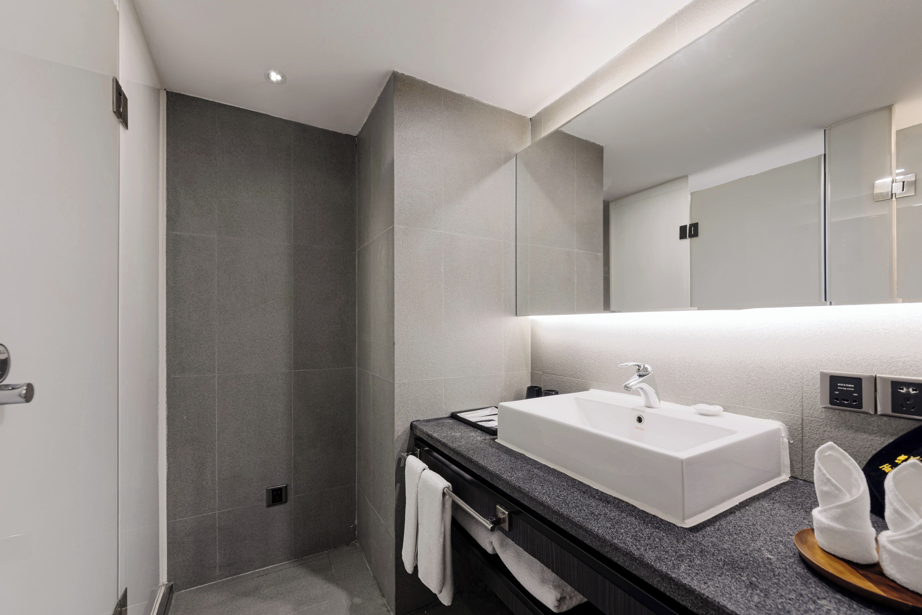 Un baño moderno con un lavamanos blanco, encimera oscura y un espejo grande.