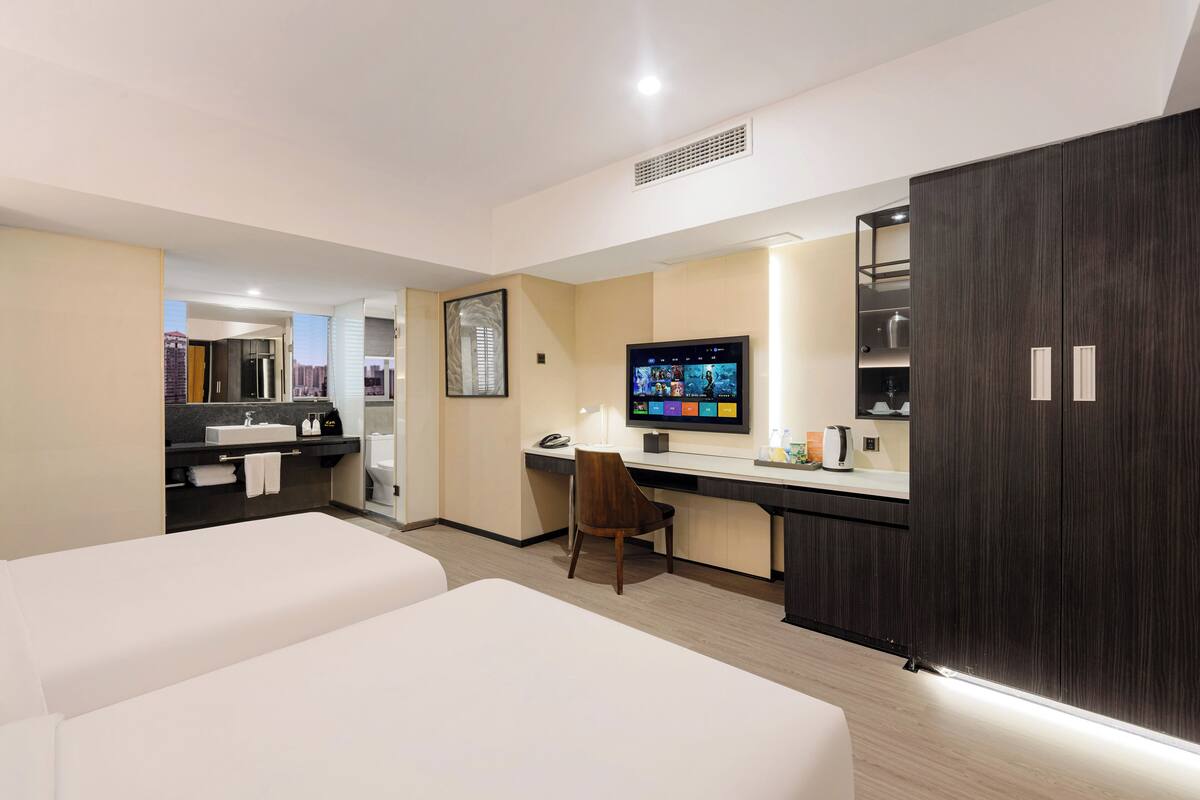 A hotel room with two beds, a desk with a computer, a TV, and a minibar.