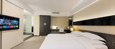 A modern hotel room with a large bed, a desk, a chair, a TV mounted on the wall, and a bedside lamp.