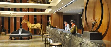 Un vestíbulo con mostrador de recepción, una gran escultura de madera en forma de caballo y un diseño moderno de techo.