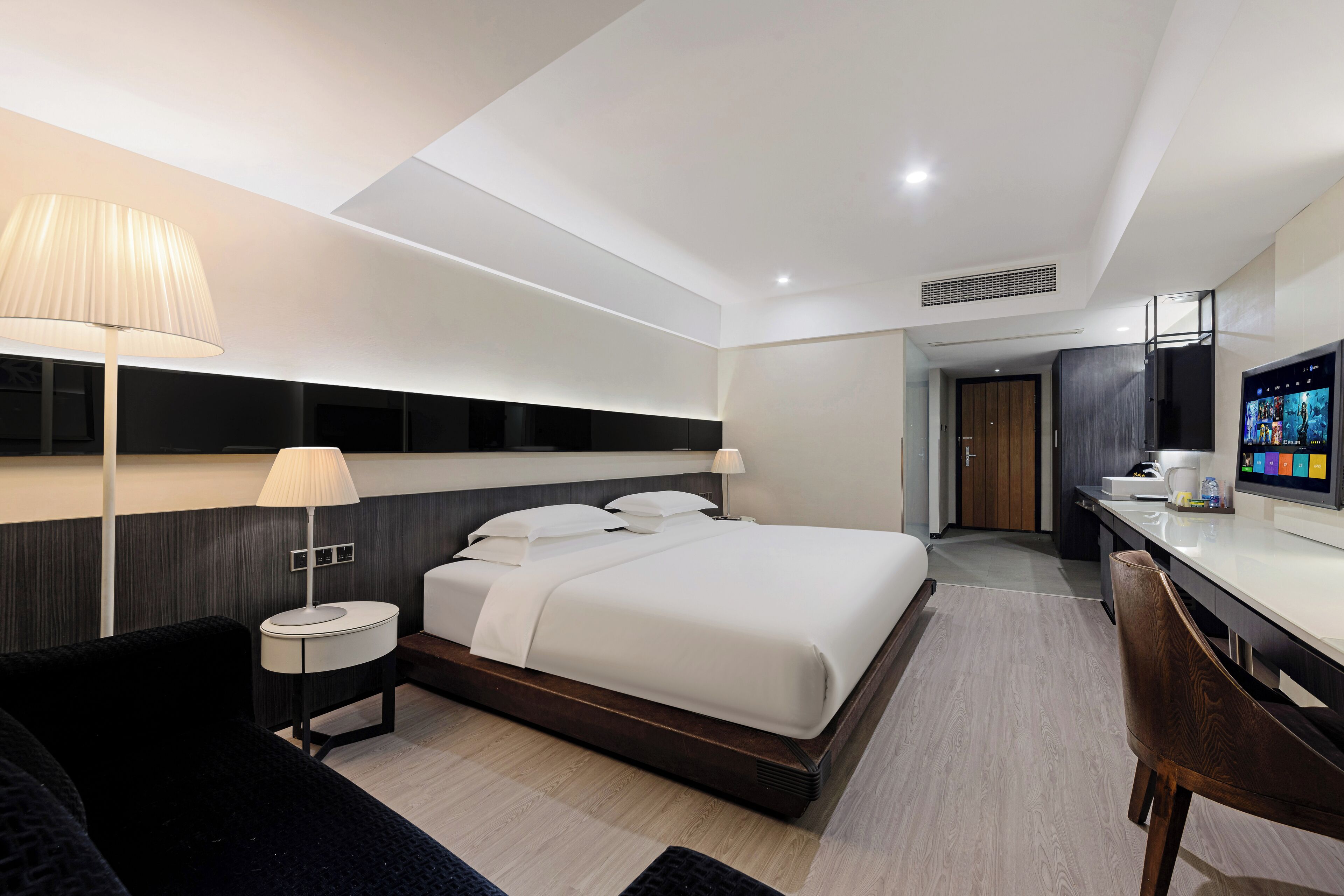 A modern hotel room with a large bed, bedside tables, a desk, and a TV.