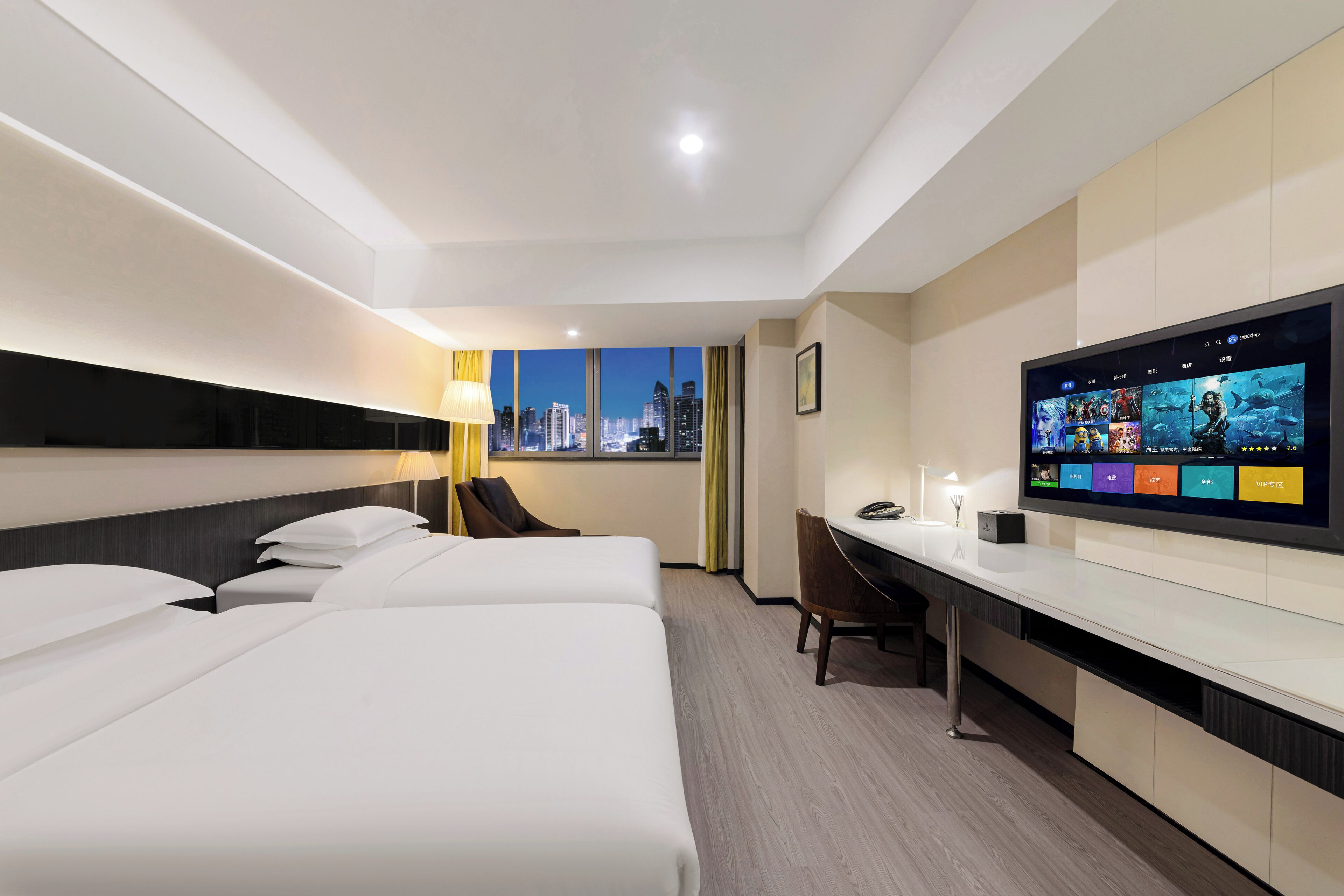 Habitación de hotel con tres camas, un escritorio, televisión y vista a la ciudad.