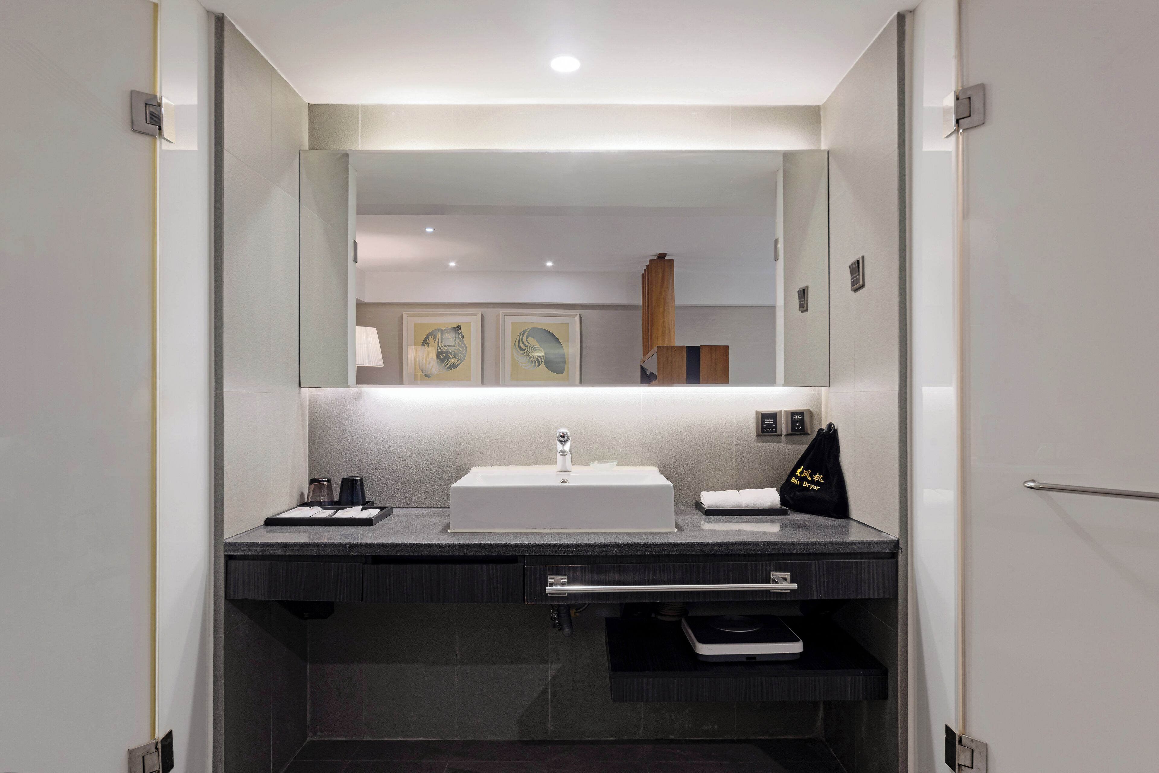 A modern bathroom with a large mirror, a white sink, and a dark countertop. There are two framed pictures on the wall above the mirror.
