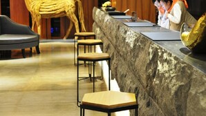 Uma área de recepção com balcão de mármore, banquetas de madeira e uma grande escultura de cavalo.