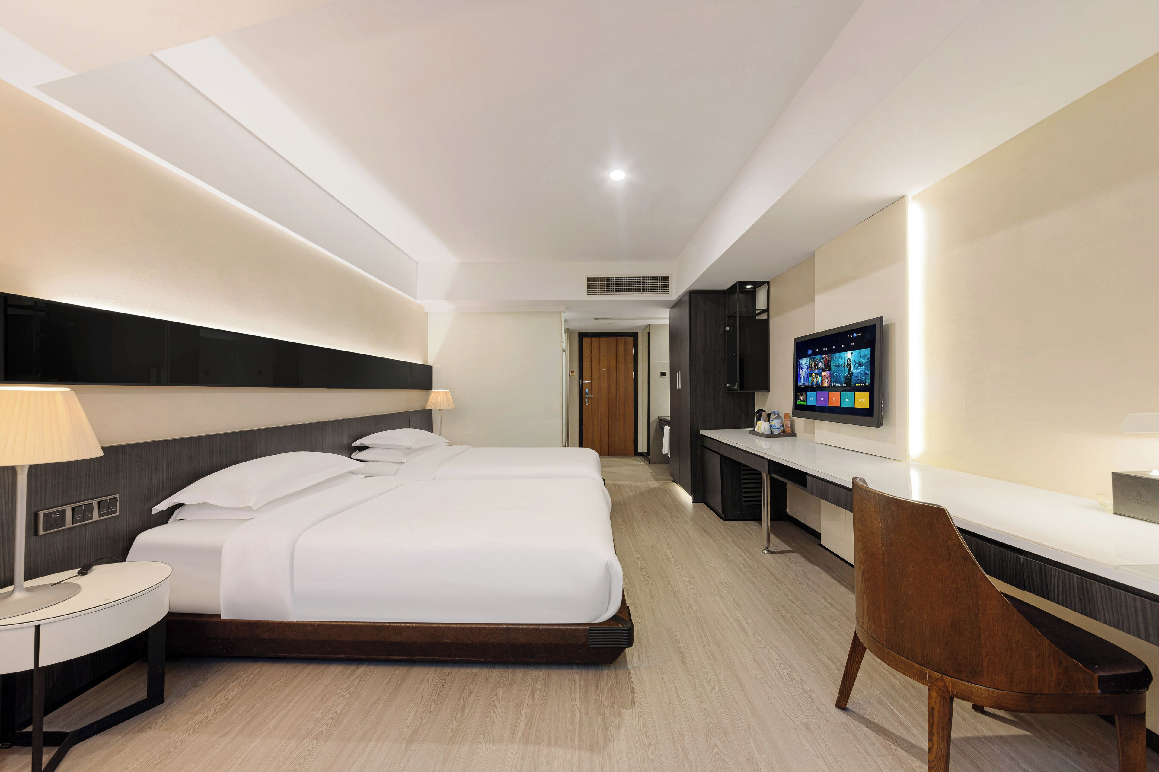 A hotel room with a large bed, a desk, a chair, a TV, and a lamp.