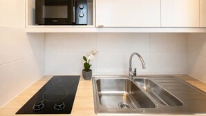 A modern kitchen with a black induction cooktop, a stainless steel sink, and a microwave on a white cabinet shelf. - Family flat -  Montparnasse (Paris)