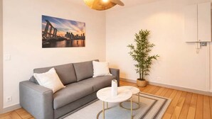 A modern living room with a grey sofa, a round coffee table, a hanging lamp, a cityscape painting, and a bamboo plant. - Family flat -  Montparnasse (Paris)