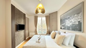 A modern bedroom with a bed, a TV, a large window, and a cityscape painting. - Unique Parisian flat near Gare Montparnasse (Paris)