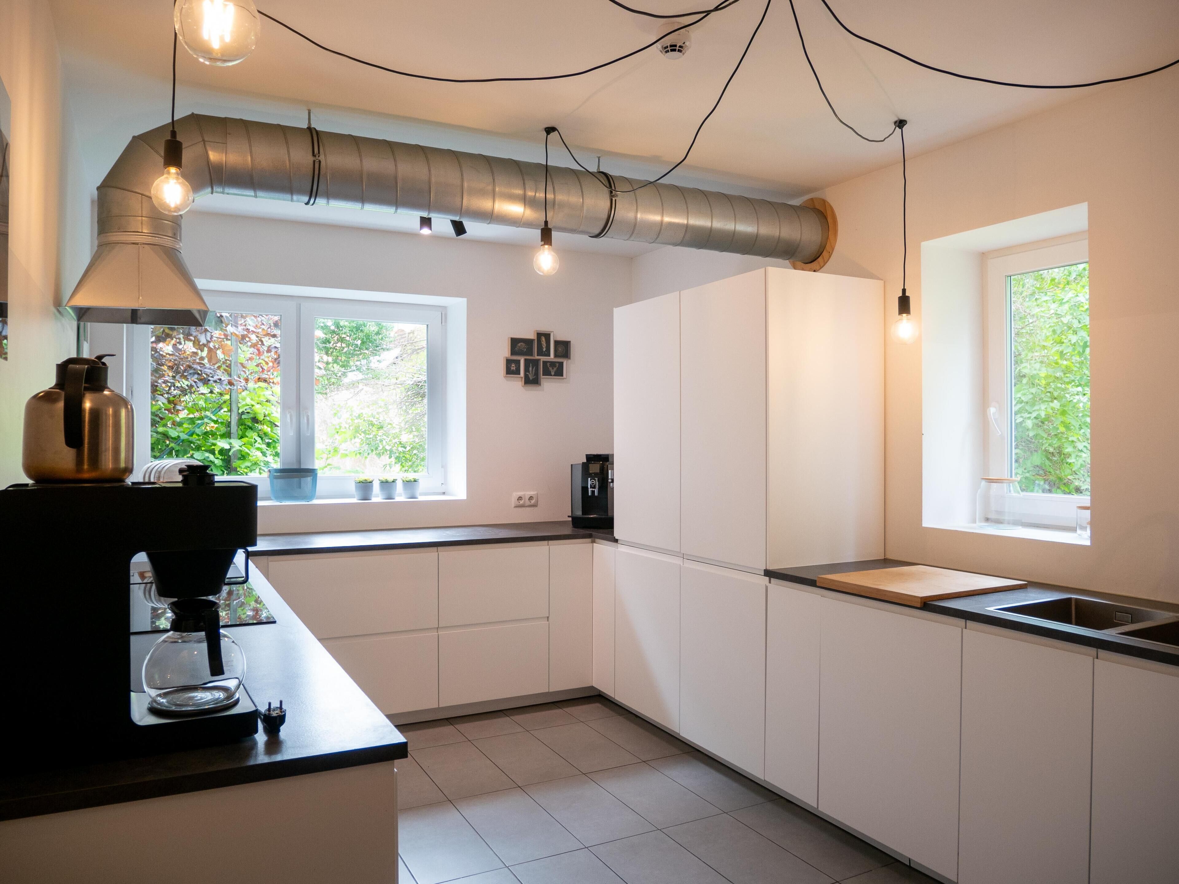 Cocina moderna con armarios blancos, encimera negra, cafetera y ventana con vistas a zonas verdes.