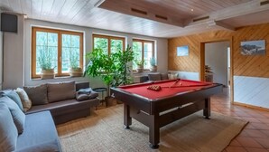 Una habitación acogedora con mesa de billar, sofá y ventanas amplias.