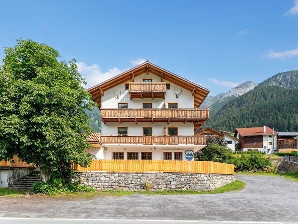 Ein mehrstöckiges Gebäude mit Balkonen, einer Steinmauer und einer Bergkulisse im Hintergrund.