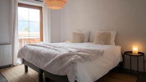 Un dormitorio con cama, una mesita de noche con lámpara, ventana con cortinas y una lámpara colgante.