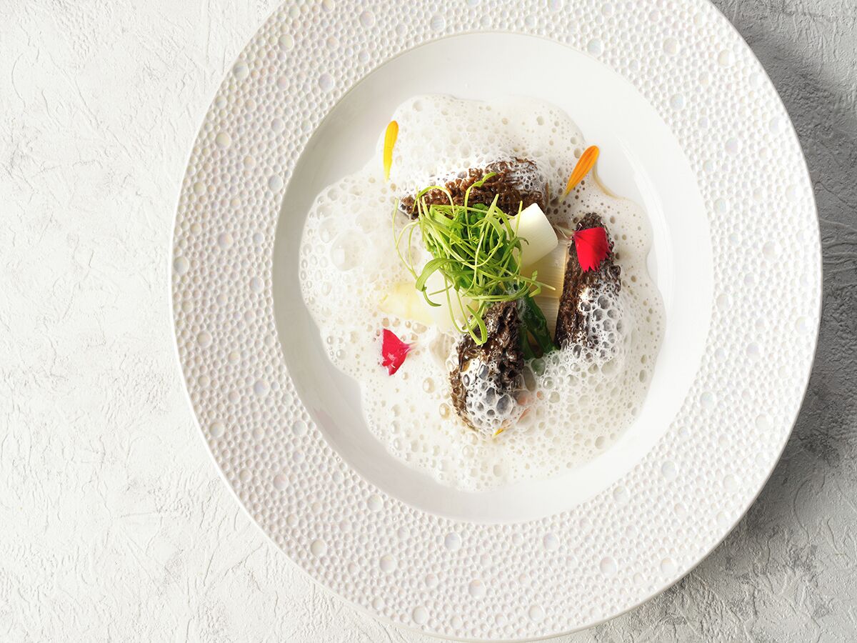 A white plate with a dish on a textured white surface.