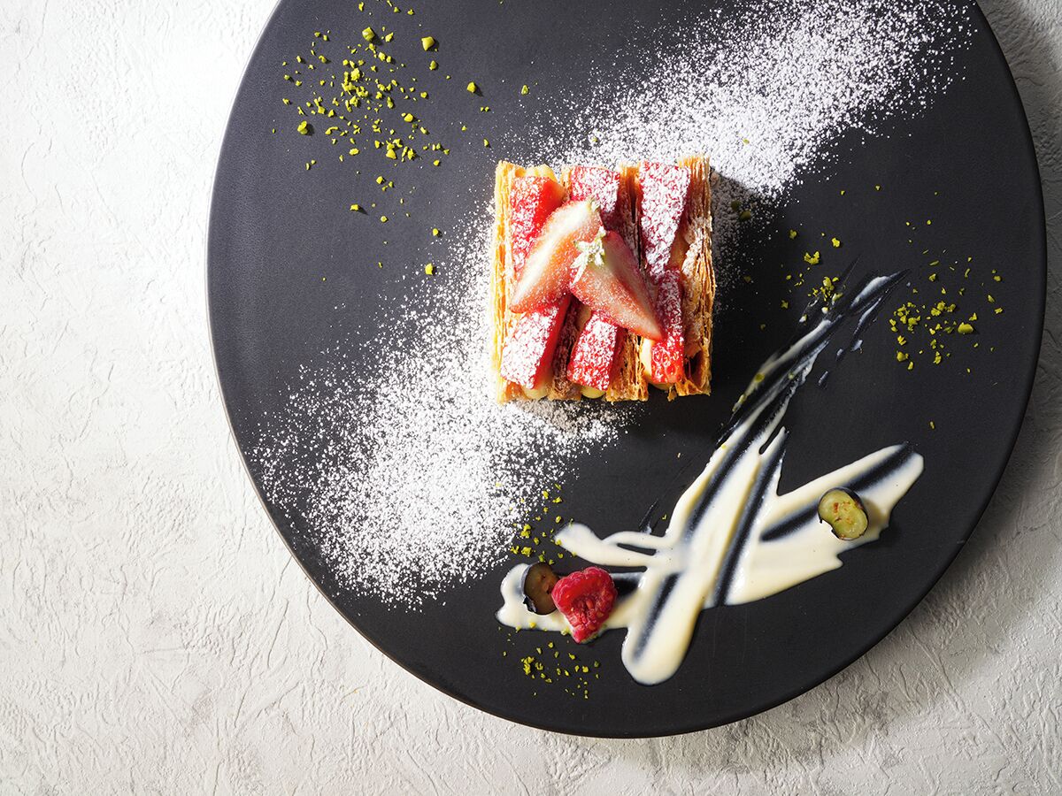 A dessert on a black plate with powdered sugar and scattered pistachios.