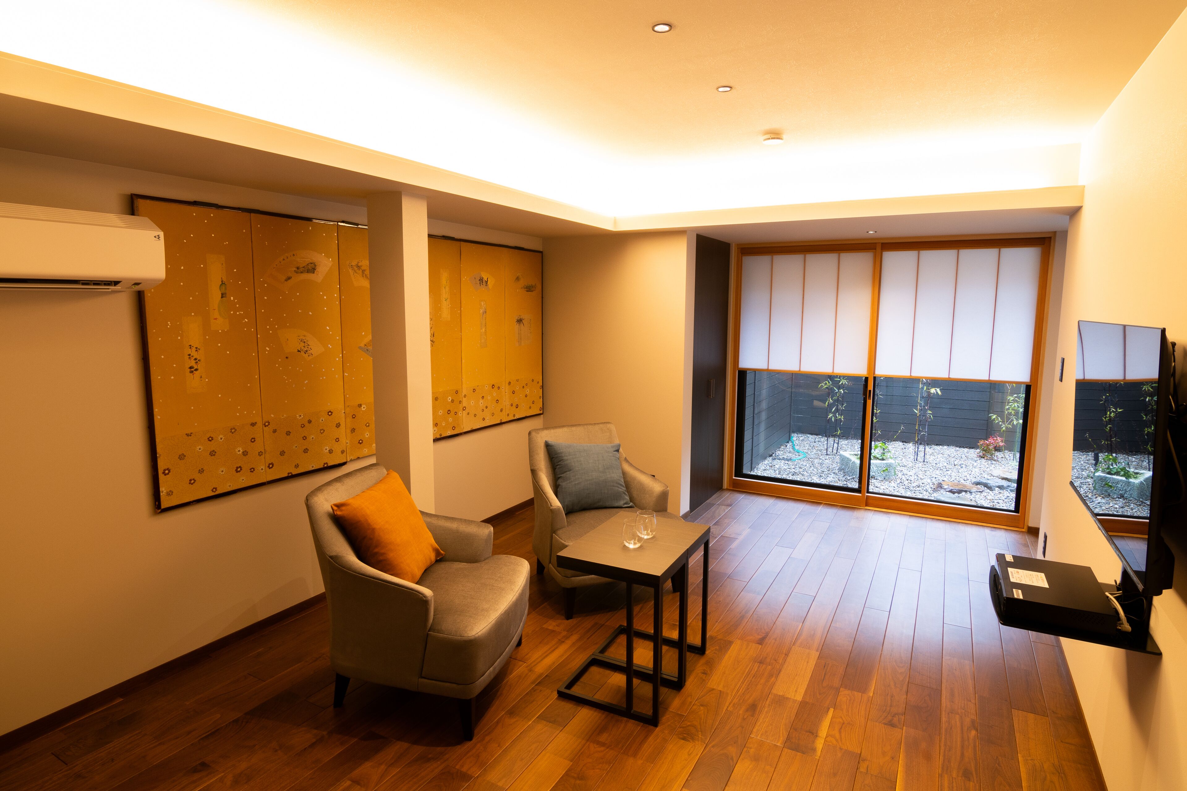A modern living room with a sofa, armchair, and coffee table. There is a large window with a view of the outside.