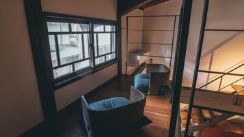 A room with a large window, a wooden floor, a wicker chair, and a metal shelf unit.