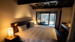 A large bed with white linens, a wooden headboard, and a nightstand with a lamp. There is a window with a view of the outdoors. - Auberge Homachi Mikuniminato (Sakai)