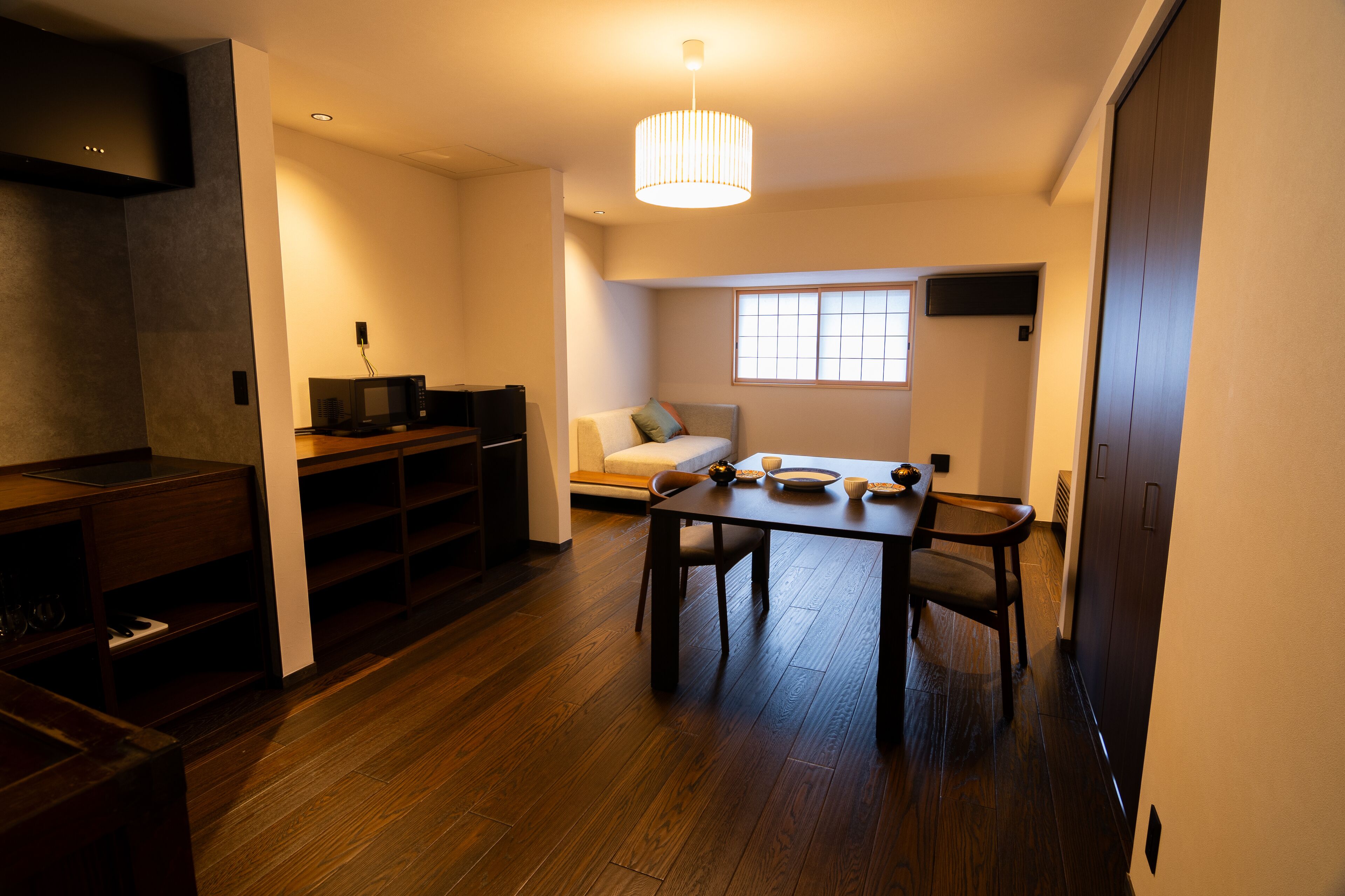 Una sala de estar moderna con comedor, piso de madera, un sofá, un televisor y una mesa con sillas.