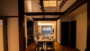 A dining area with a wooden table and chairs, a view of the outdoors through a window, and a traditional Japanese interior design. - Auberge Homachi Mikuniminato (Sakai)