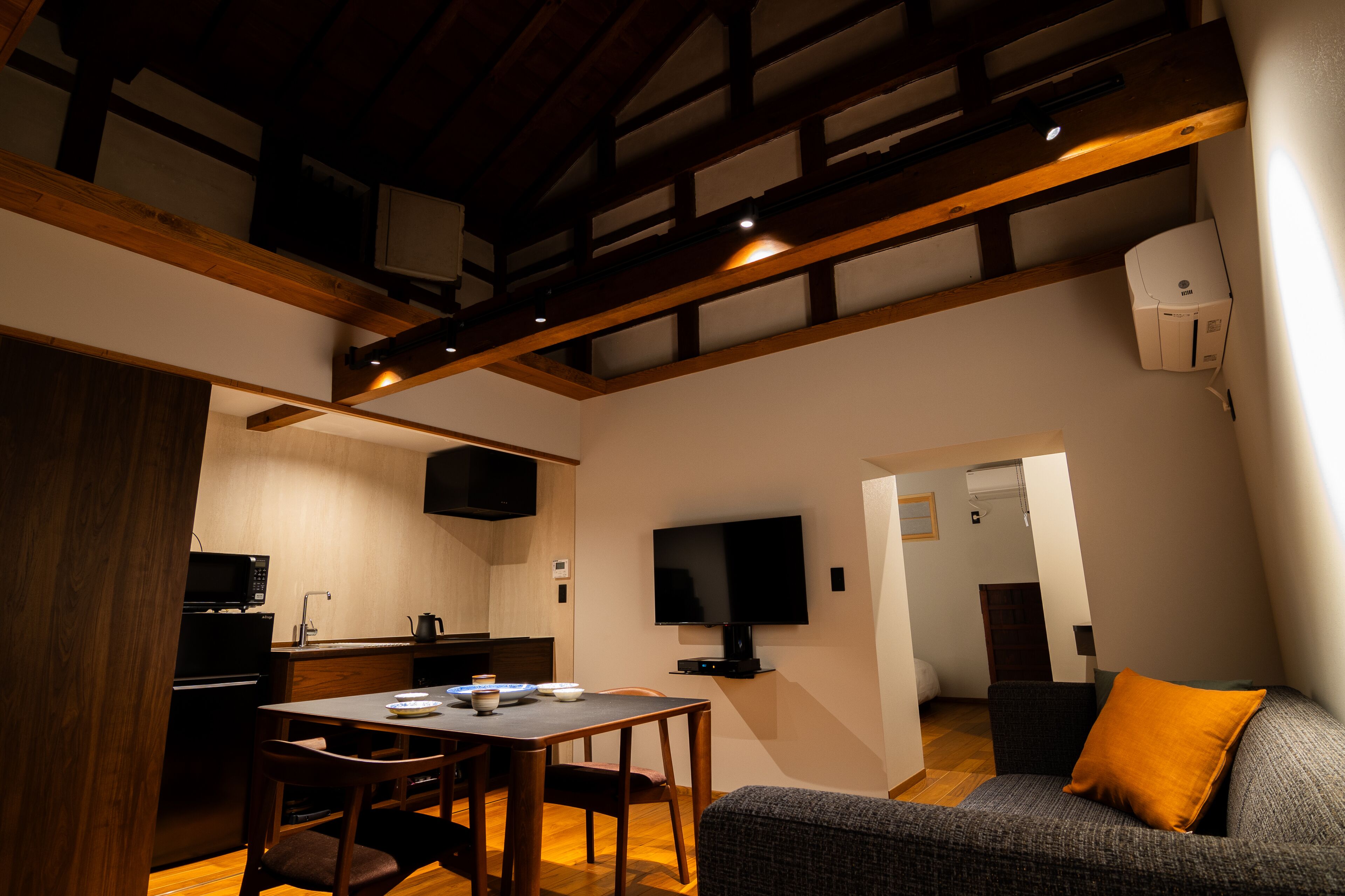 A compact living space with a dining area, kitchenette, and a TV mounted on the wall.
