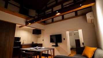 A compact living space with a dining area, kitchenette, and a TV mounted on the wall.